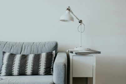 white study lamp on top of white wooden end table beside gray fabric sofa